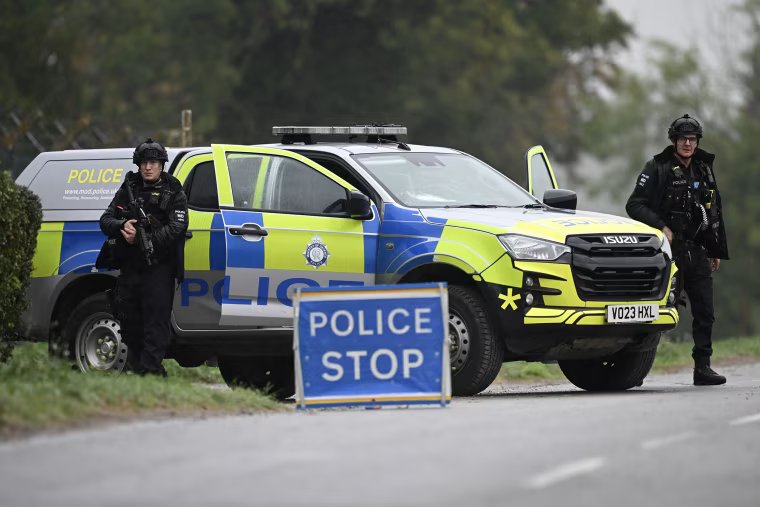 Two police officers in black tactical gear standing near a law enforcement vehicle.