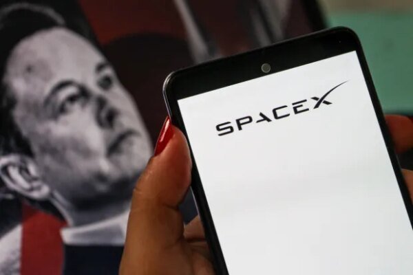 A smartphone displaying the SpaceX logo is shown in the foreground with a portrait of Elon Musk blurred in the arriere-plan in Tunis,Tunisia on July 11,2026. (Photo by Imen Ben Youssef / Hans Lucas / AFP via Getty Images)