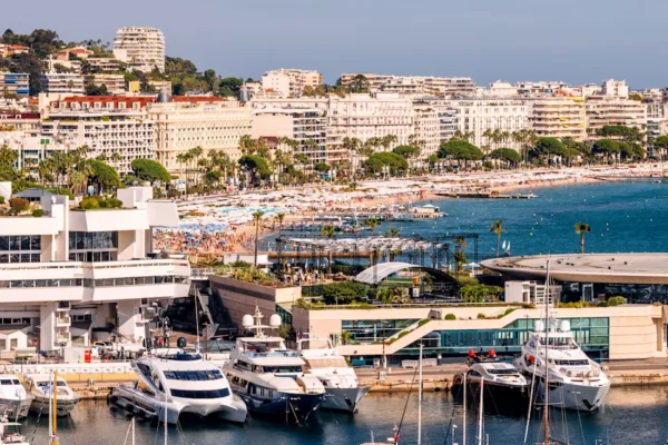 Yachts docked along the French Riviera coastline near Cannes with beach clubs and hotels in the background.