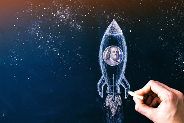 A human hand drawing a rocket with Benjamin Franklin's face in the center.