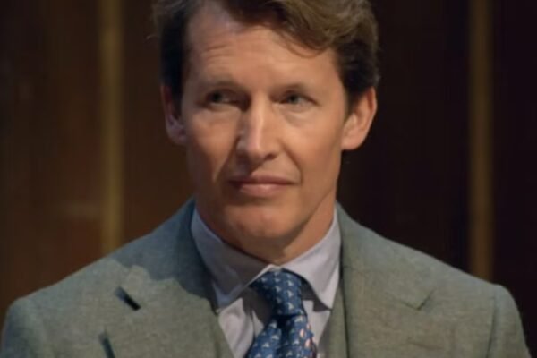 person in a suit with a blue patterned tie, looking to the side.