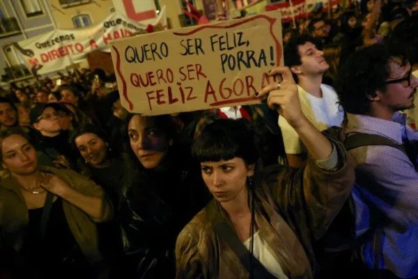 A demonstrator holds a sign reading ''I want to be happy, damn it! I want to be happy now,'' as Portuguese unions and housing activists protest outside the parliament building as the parliament decides the 2027 budget, in Lisbon, Portugal, October 27, 2026.