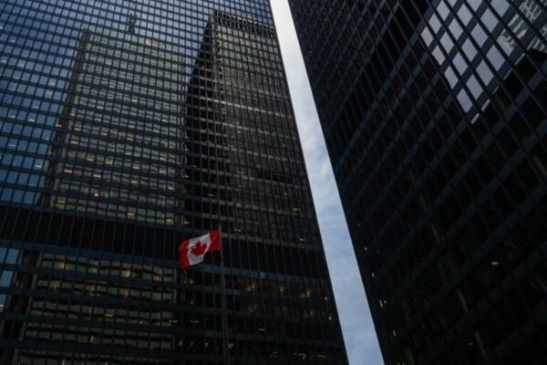An image of the Canadian flag against two tall buildings with glass windows in the background.