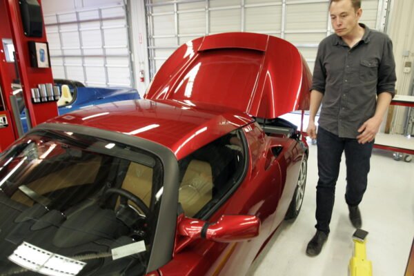 Tesla CEO Elon Musk walks next to a new Tesla sports car at a showroom