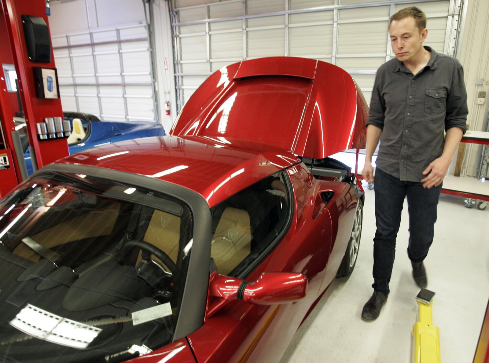 Tesla CEO Elon Musk walks next to a new Tesla sports car at a showroom