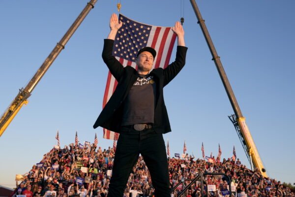 A man in a baseball cap takes the stage at a political rally.
